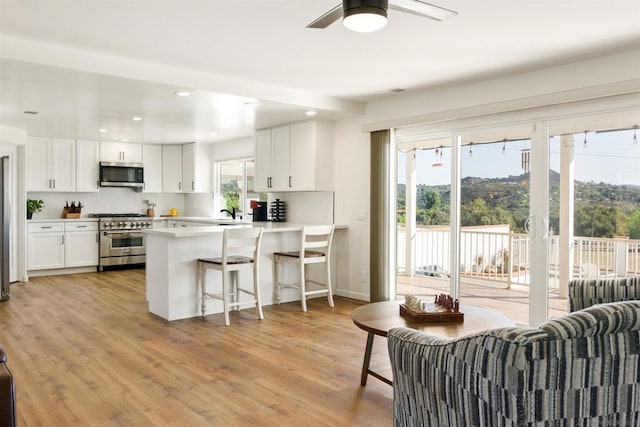 kitchen featuring kitchen peninsula, light wood-type flooring, white cabinets, appliances with stainless steel finishes, and a kitchen breakfast bar