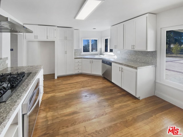 kitchen featuring white cabinetry, light stone counters, dark hardwood / wood-style floors, range hood, and appliances with stainless steel finishes