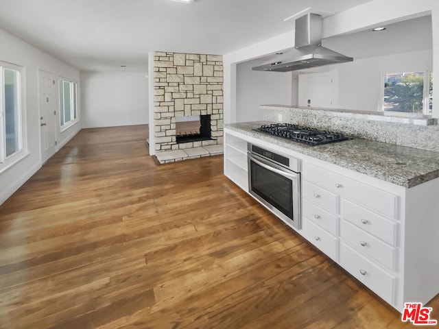 kitchen featuring white cabinets, stainless steel oven, gas cooktop, light stone counters, and island exhaust hood