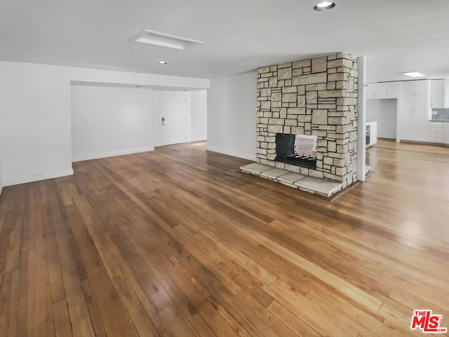 unfurnished living room with wood-type flooring and a stone fireplace