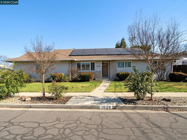 ranch-style home featuring a front lawn and solar panels