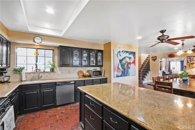 kitchen with a raised ceiling, appliances with stainless steel finishes, ceiling fan, sink, and backsplash