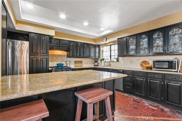 kitchen featuring light stone counters, a raised ceiling, a breakfast bar, decorative backsplash, and appliances with stainless steel finishes