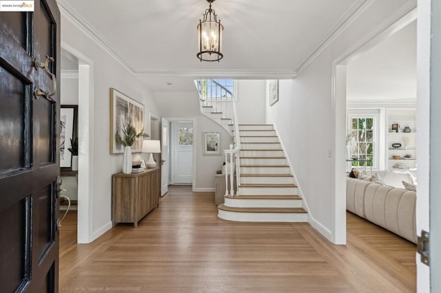 foyer featuring light hardwood / wood-style flooring, ornamental molding, and an inviting chandelier