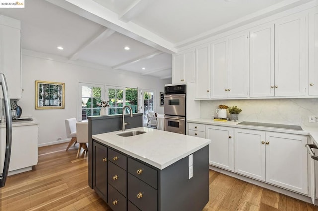 kitchen with beamed ceiling, white cabinetry, sink, and an island with sink