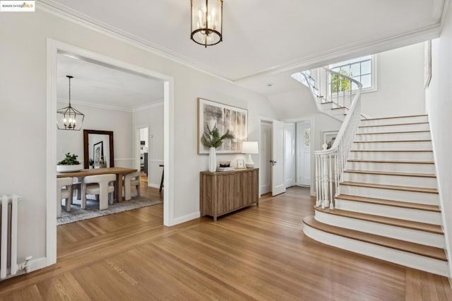 foyer with wood-type flooring, radiator heating unit, ornamental molding, and an inviting chandelier