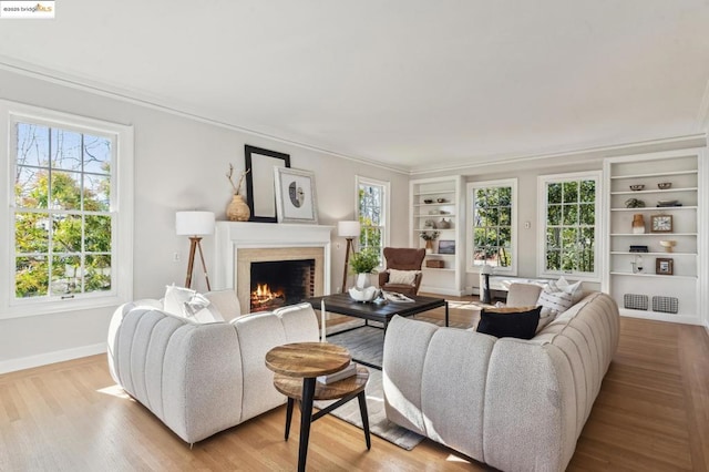 living room with light wood-type flooring, built in features, plenty of natural light, and ornamental molding