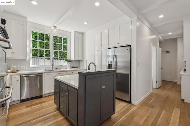 kitchen with a center island with sink, beam ceiling, sink, appliances with stainless steel finishes, and white cabinets