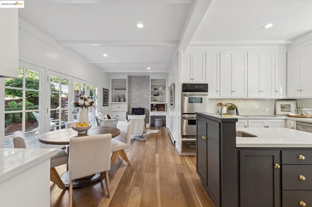 kitchen with beamed ceiling, sink, light wood-type flooring, white cabinets, and double oven