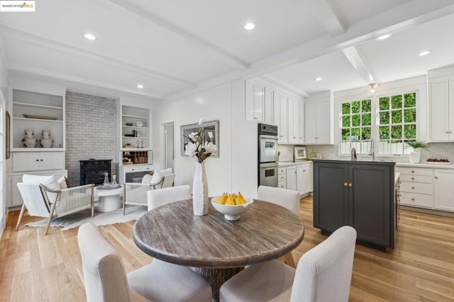 dining area with a brick fireplace, beam ceiling, and light hardwood / wood-style flooring