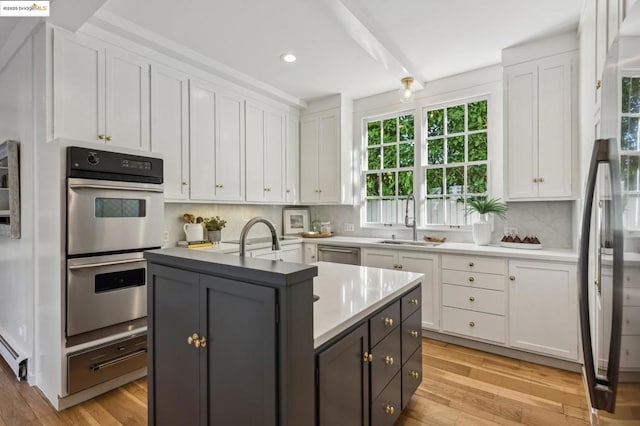 kitchen with white cabinetry, an island with sink, appliances with stainless steel finishes, decorative backsplash, and sink