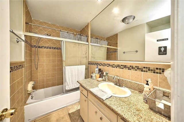 bathroom with tiled shower / bath, tile patterned flooring, vanity, tasteful backsplash, and tile walls