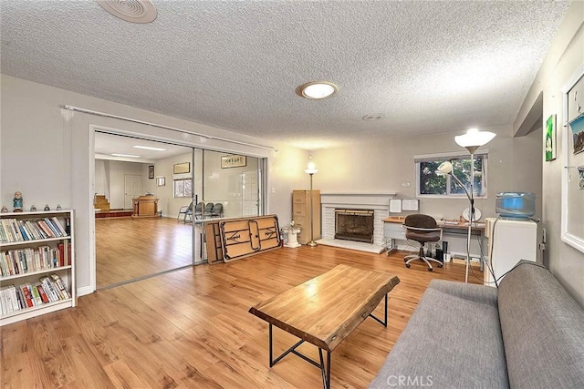 living room featuring wood-type flooring, a textured ceiling, and a brick fireplace