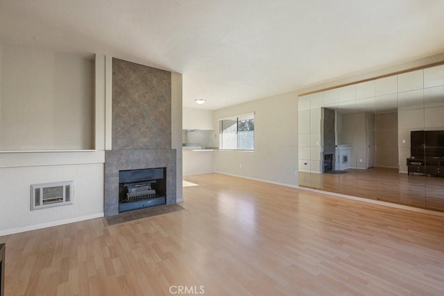 unfurnished living room featuring baseboards, a tile fireplace, wood finished floors, and heating unit