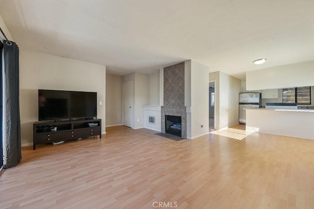 unfurnished living room with light wood-type flooring, visible vents, a fireplace, and baseboards