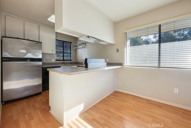 kitchen featuring light countertops, freestanding refrigerator, light wood-type flooring, a peninsula, and dishwashing machine