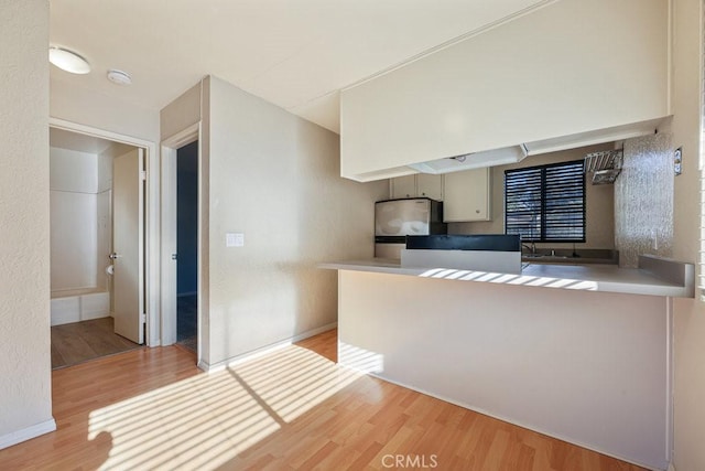 kitchen featuring baseboards, freestanding refrigerator, a peninsula, light wood-style floors, and a sink