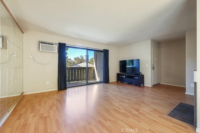 unfurnished living room with light wood-style flooring, baseboards, and a wall mounted AC