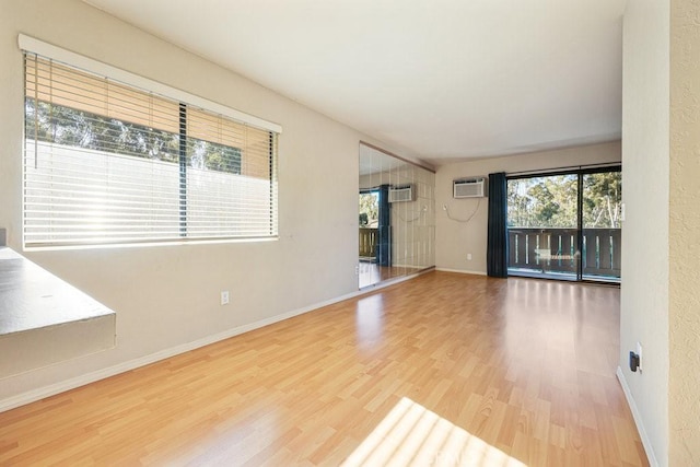 unfurnished room featuring a wall mounted air conditioner, baseboards, and wood finished floors