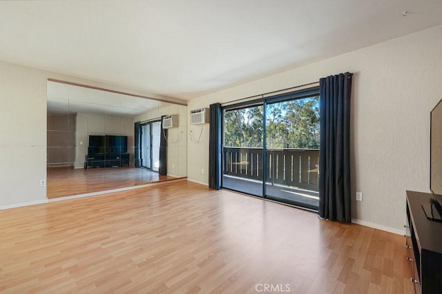 unfurnished living room featuring a textured wall, an AC wall unit, wood finished floors, and baseboards