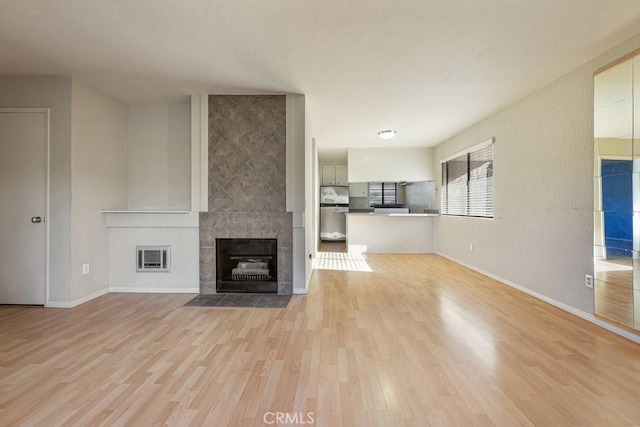 unfurnished living room featuring light wood-type flooring, baseboards, and a tiled fireplace