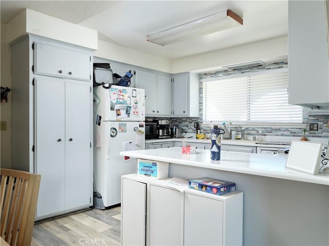 kitchen with white fridge, decorative backsplash, light hardwood / wood-style floors, and kitchen peninsula