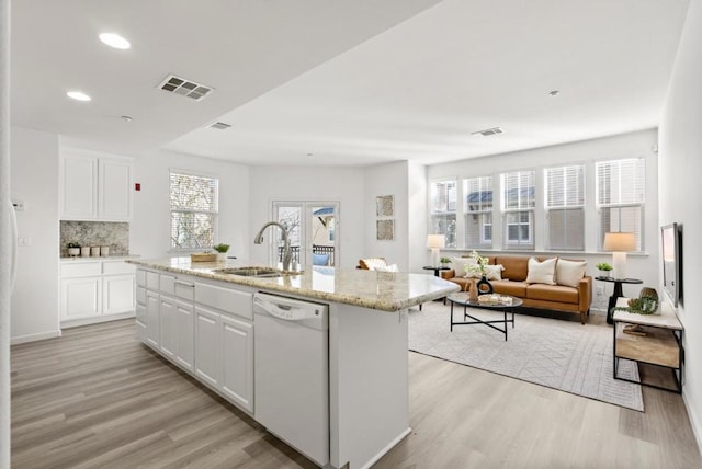 kitchen with white dishwasher, sink, backsplash, white cabinetry, and a kitchen island with sink