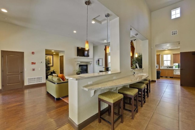 kitchen with light stone countertops, a towering ceiling, decorative light fixtures, kitchen peninsula, and a breakfast bar