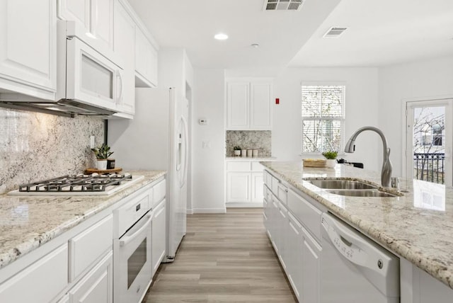 kitchen with light stone countertops, white appliances, white cabinets, tasteful backsplash, and sink