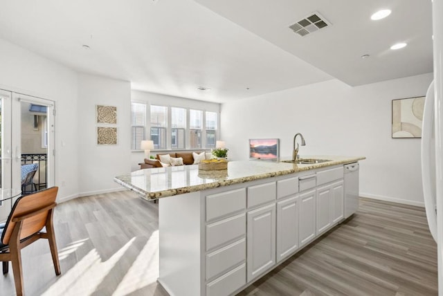 kitchen with dishwasher, white cabinetry, a kitchen island with sink, sink, and light hardwood / wood-style flooring