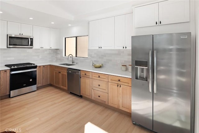 kitchen featuring backsplash, light countertops, light wood-style floors, stainless steel appliances, and a sink