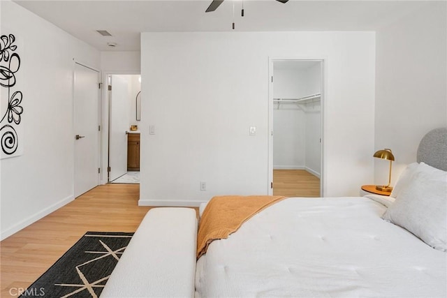 bedroom featuring a walk in closet, a ceiling fan, wood finished floors, a closet, and baseboards