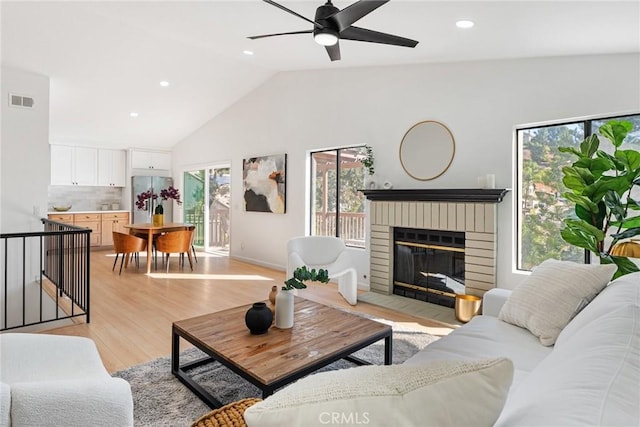 living room featuring ceiling fan, a brick fireplace, light wood-type flooring, and plenty of natural light