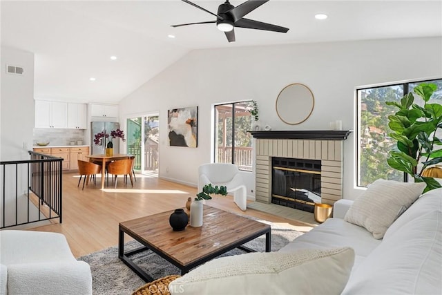 living area with visible vents, a brick fireplace, light wood-type flooring, lofted ceiling, and recessed lighting