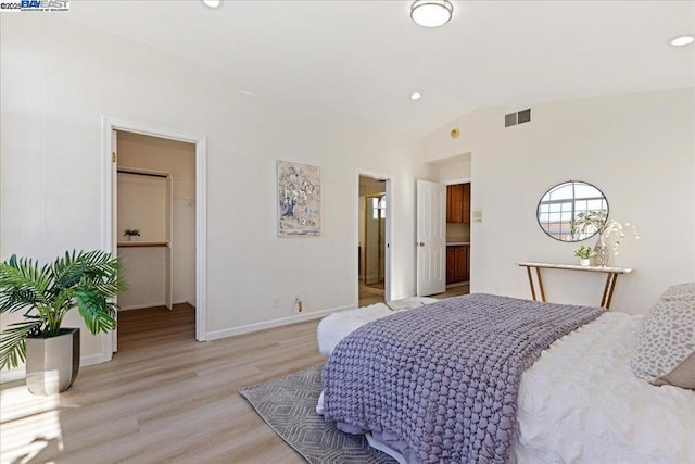 bedroom featuring ensuite bath, a walk in closet, vaulted ceiling, and light hardwood / wood-style flooring