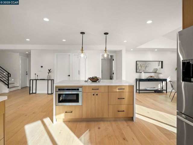 kitchen featuring stainless steel appliances, light brown cabinetry, light wood-type flooring, and hanging light fixtures