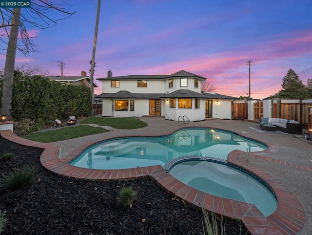 back house at dusk featuring a pool with hot tub, a patio area, and an outdoor living space