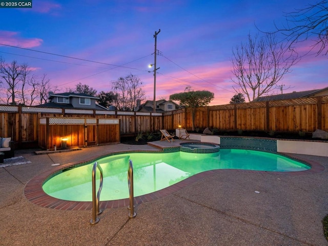 pool at dusk featuring a patio area and an in ground hot tub