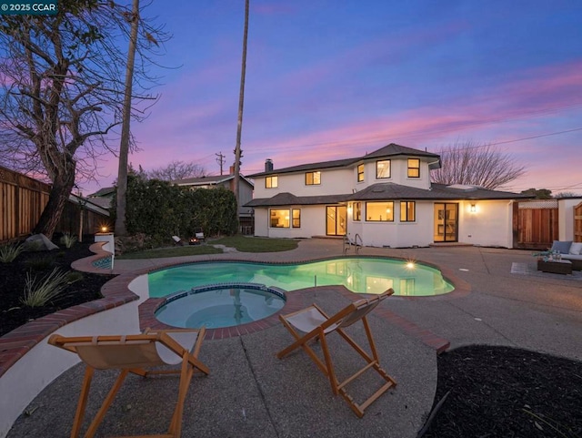 pool at dusk with an in ground hot tub and a patio area