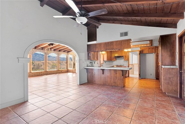 kitchen with a kitchen bar, ceiling fan, light tile patterned floors, tasteful backsplash, and kitchen peninsula