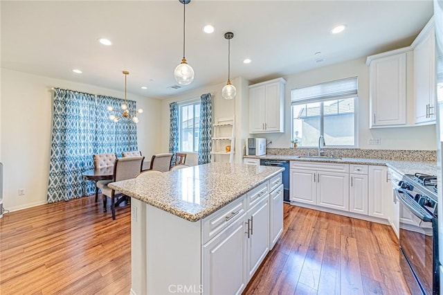 kitchen with sink, white cabinetry, hanging light fixtures, a kitchen island, and black appliances