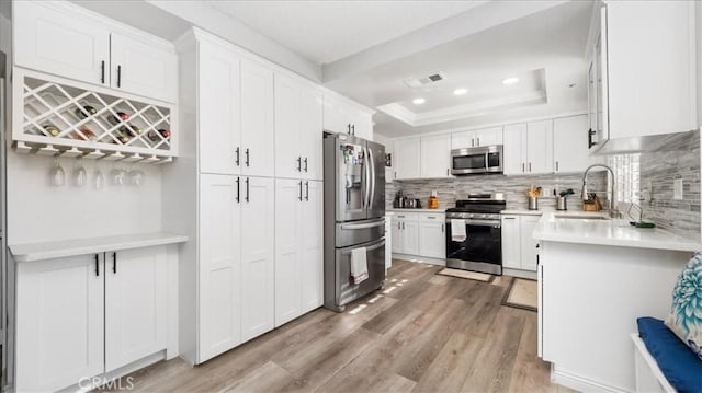 kitchen with stainless steel appliances, sink, white cabinetry, light hardwood / wood-style floors, and a tray ceiling