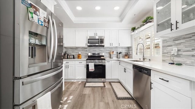 kitchen with sink, white cabinets, a raised ceiling, light wood-type flooring, and appliances with stainless steel finishes