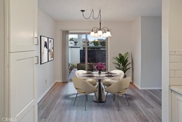 dining space with a textured ceiling, light hardwood / wood-style flooring, and a chandelier