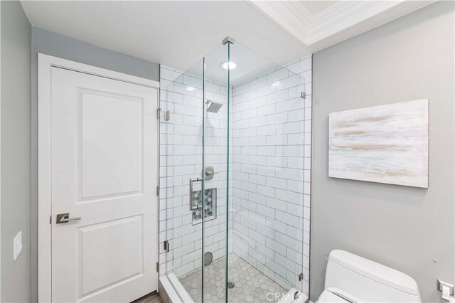 bathroom featuring toilet, a shower with shower door, and crown molding