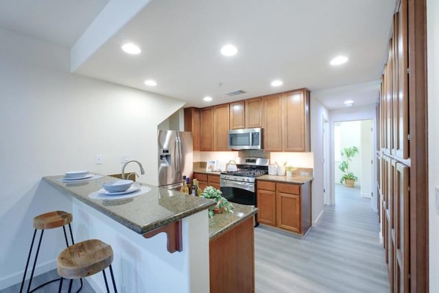 kitchen featuring light hardwood / wood-style floors, kitchen peninsula, appliances with stainless steel finishes, stone countertops, and a breakfast bar