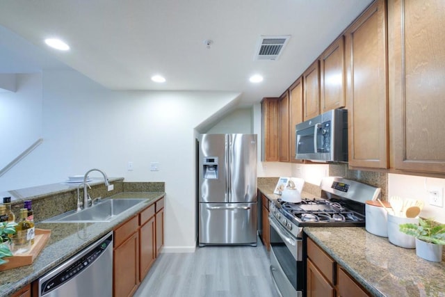 kitchen featuring light hardwood / wood-style floors, stainless steel appliances, backsplash, stone counters, and sink