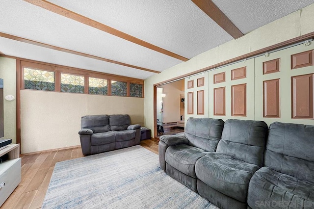 living room with a textured ceiling, beamed ceiling, and light hardwood / wood-style flooring