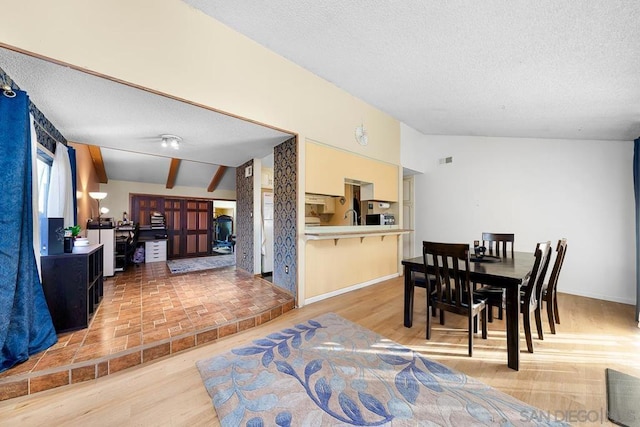 dining room featuring a textured ceiling, light hardwood / wood-style flooring, vaulted ceiling with beams, and sink