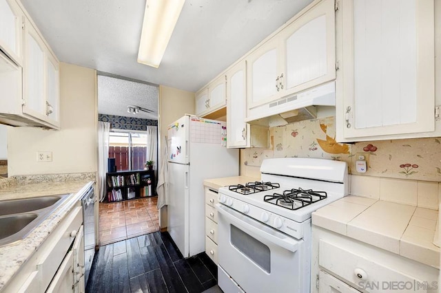 kitchen featuring white appliances, a textured ceiling, tile counters, and white cabinetry